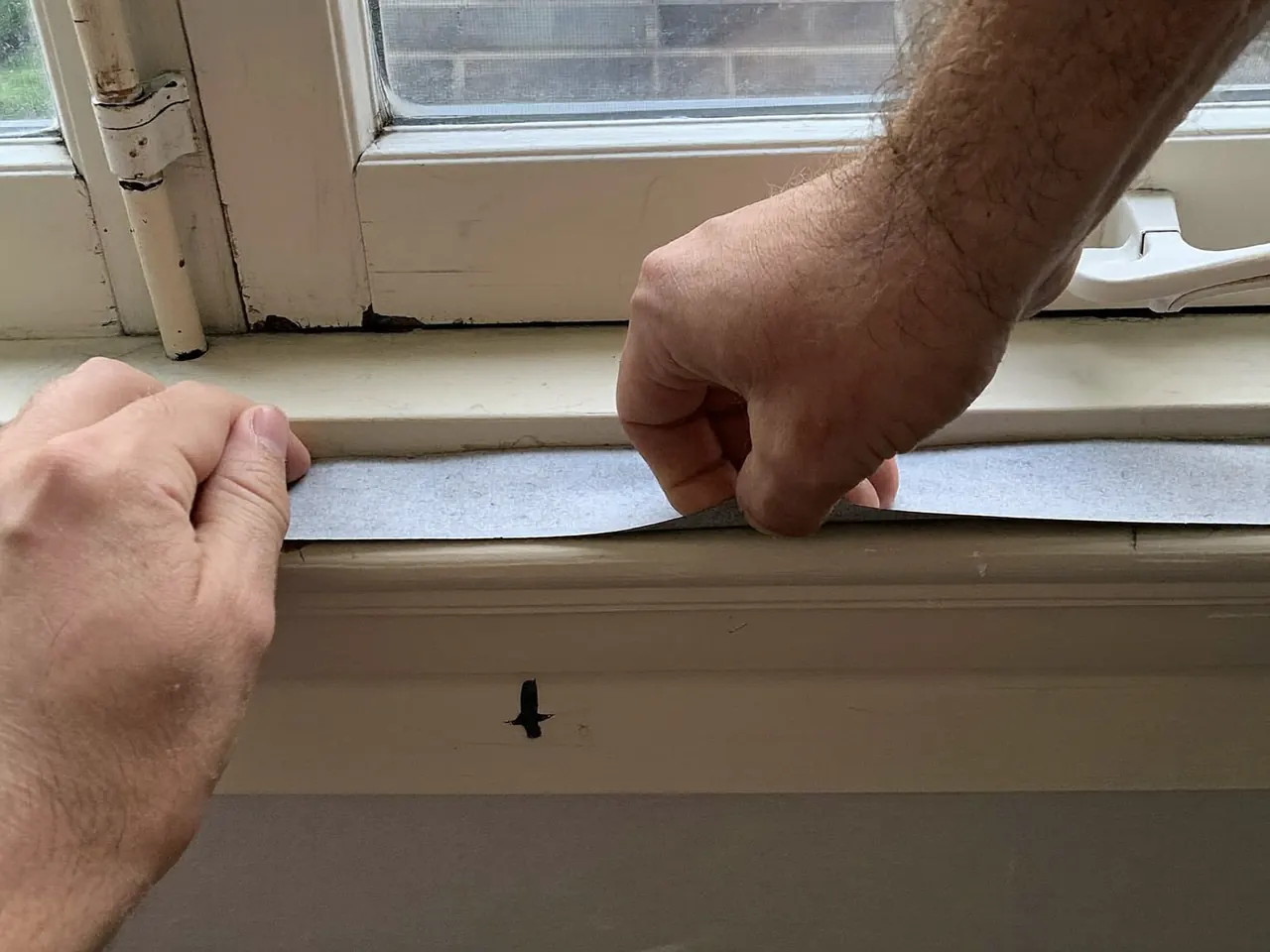 Hand fitting a draught-proofing seal strip along the edge of a window frame