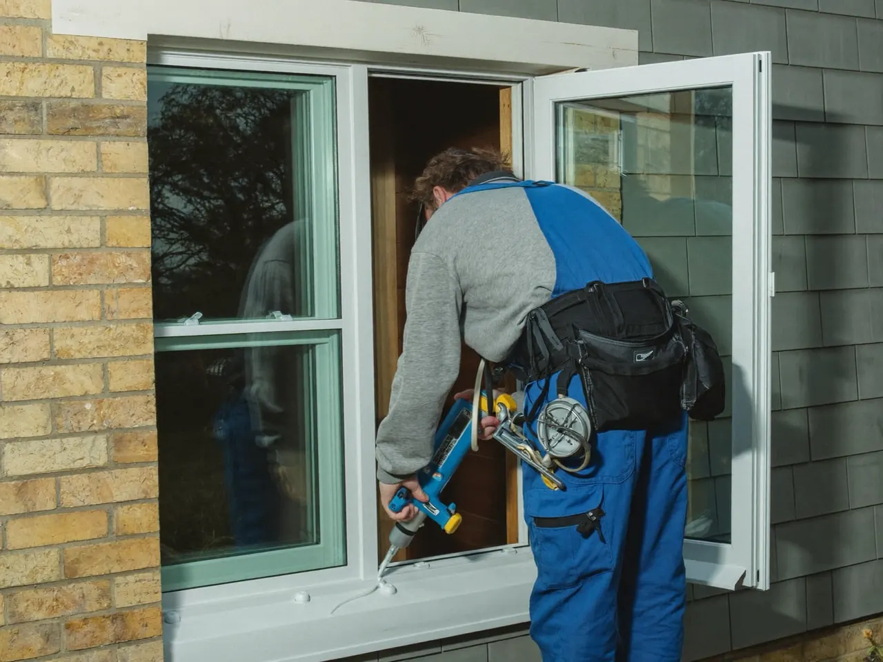 Installer fitting a new double-glazed window into a home and sealing the frame
